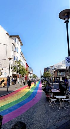 a rainbow painted street with people sitting at tables and walking down the sidewalk in front of buildings