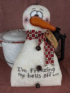 a snowman with a hat and scarf next to a white bowl on a red checkered table cloth