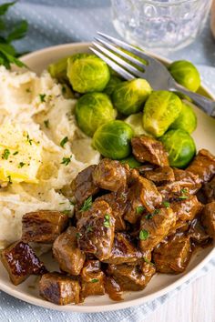 a white plate topped with meat and potatoes next to brussel sprouts