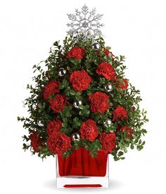 red carnations and greenery are arranged in a square vase with snowflakes on top