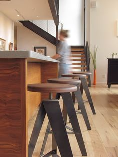 three stools in front of a counter with a person walking up the stairs behind them