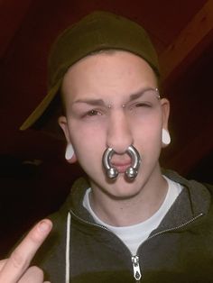 a young man with piercings on his nose is making the middle finger sign for the camera