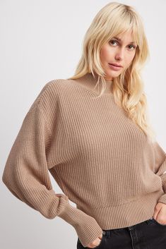 a woman wearing a tan sweater and black jeans is standing with her hands on her hips