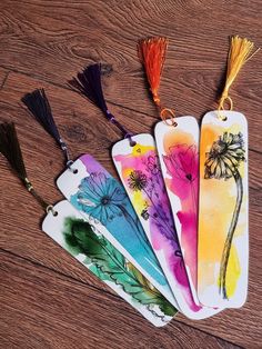 four tags with flowers painted on them sitting on a wooden table next to tassels