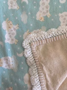 a baby blanket with crocheted edges and sheeps on it, sitting on top of a bed