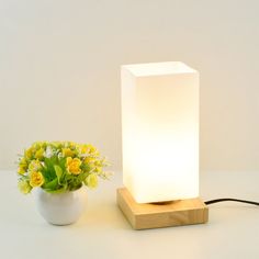 a white vase with yellow flowers next to a wooden block shaped lamp on a table