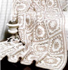 a white crocheted blanket sitting on top of a bed next to a vase