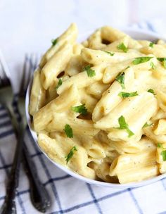 a white bowl filled with pasta and parsley on top of a blue checkered table cloth