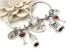 two key chains with wine charms attached to them on a white surface next to a flower