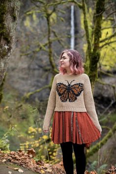 a woman standing in the woods wearing a sweater with a butterfly on it's back