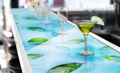 two martini glasses sitting on top of a counter next to each other with lime slices