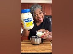 an older woman holding a container of mayonnaise next to a mixing bowl