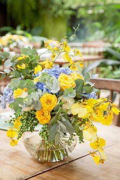 a vase filled with yellow and blue flowers sitting on top of a wooden dining table