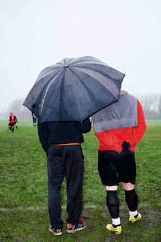 two people standing under an umbrella in the rain on a soccer field with other players