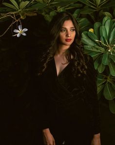 a woman is standing in front of some leaves and flowers with her hands on her hips