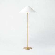 a gold floor lamp with a white shade on the base and a brass plated base