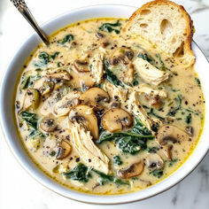 a white bowl filled with chicken and spinach soup next to a slice of bread