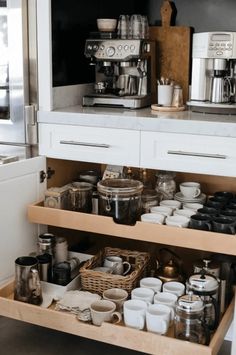 an open drawer in a kitchen with pots and pans on the shelves, next to a coffee maker