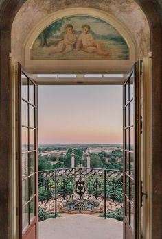 an open door leading to a balcony with paintings on the walls and doors that lead out onto a lush green landscape