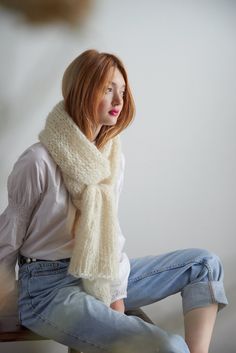 a woman sitting on top of a wooden bench wearing a white scarf and blue jeans