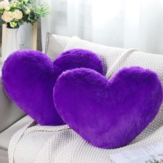 two purple heart shaped pillows sitting on top of a couch