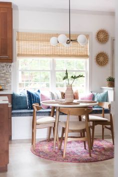 a dining room table with chairs and a bench in front of a window that is decorated with colorful pillows