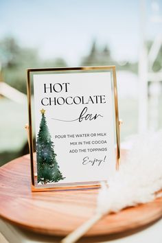 a hot chocolate bar sign sitting on top of a wooden table next to a white feather