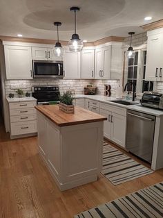 a kitchen with white cabinets and wooden counter tops, an island in front of the stove