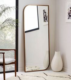 a large mirror sitting on top of a white rug next to a chair and potted plant