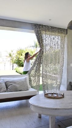 a woman standing in front of a living room window next to a couch and coffee table