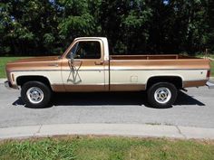 a tan and brown truck parked in a parking lot next to some trees on a sunny day