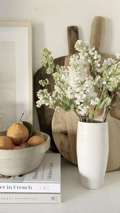 a white vase filled with flowers and oranges next to a cutting board on a table