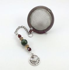 a tea strainer and keychain on a white surface with a bead chain