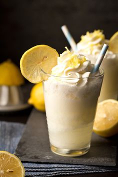 two glasses filled with lemonade and whipped cream next to sliced lemons on a napkin