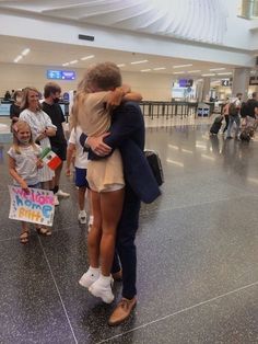 two people hugging each other in an airport terminal with luggage and signs on the floor