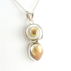 Malabar shell and bronze baroque pearl is handmade with sterling silver in Bali, Indonesia. A nice 1/4 inch sterling silver bezel setting holds the pearl shell combination that hangs from an 18 inch rhodium plated sterling silver cable chain. Pendant is 1 1/2 inches long and 1/2 inch wide. Necklace comes in a jewelry gift box. Style Number: 6689 Metal: 925 Sterling Silver Gemstone: Genuine Malabar Shell and Nautilus Shell Dimensions: 1 1/2 inches long and 1/2 inch wide Handmade in Bali, Indonesi Silver Shell Necklace With Pearl Pendant As Gift, Silver Shell Necklace With Pearl Pendant, Artisan Sterling Silver Pearl Pendant Jewelry, Artisan Sterling Silver Jewelry With Pearl Pendant, Artisan Silver Jewelry With Pearl Drop, Sterling Silver Shell-shaped Pearl Pendant, Silver Mother Of Pearl Shell Necklace With Pearl Pendant, Sterling Silver Pendant Necklace With High Luster, High Luster Sterling Silver Pendant Necklace