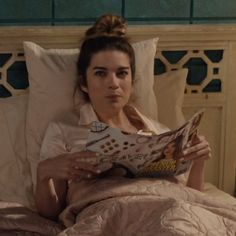 a woman laying in bed reading a magazine