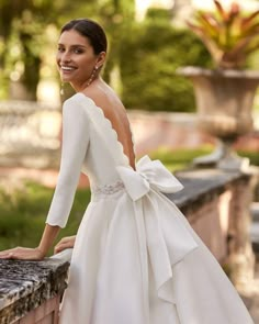 a woman in a white dress leaning on a wall