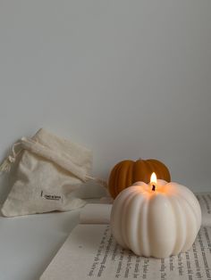 a white candle sitting on top of an open book next to a bag and paper