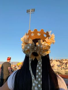 a woman wearing a crown with flowers on her head at a baseball game in the sun