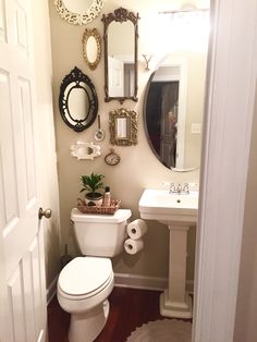 a white toilet sitting in a bathroom next to a sink under a mirror and a wooden floor