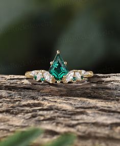 an emerald colored ring with three diamonds on it sitting on top of a piece of wood