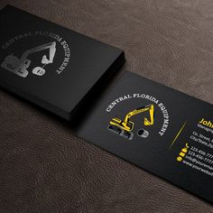 a black business card with yellow construction equipment on the front and back, sitting on top of a brown leather surface