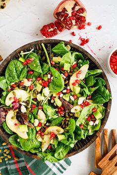 a salad with apples, spinach and pomegranates in a wooden bowl