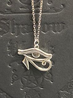 Embrace the power and mystique of ancient Egyptian symbolism with this exquisite Eye of Horus necklace. Available with either a 16-inch black cord featuring a 2-inch extension or a stainless steel chain, this necklace offers versatility and style to suit any preference. Pair it with our matching Eye of Horus earrings for a complete, coordinated look. The Eye of Horus, symbolizing protection, royal power, and good health, adds a touch of historical significance and spiritual meaning to your jewelry collection. Whether you choose the sleek black cord or the durable stainless steel chain, this necklace is perfect for everyday wear or special occasions. Features: Eye of Horus pendant Choice of 16-inch black cord with 2-inch extension or stainless steel chain Matching Eye of Horus earrings avai Symbolic Black Necklace With Adjustable Chain, Adjustable Symbolic Metal Necklace, Symbolic Adjustable Metal Necklace, Symbolic Ankh Necklace Adjustable, Symbolic Ankh Necklace, Spiritual Adjustable Engraved Charm Necklaces, Adjustable Symbolic Engraved Necklace, Adjustable Silver Ankh Necklace, Spiritual Engraved Charm Necklace, Adjustable