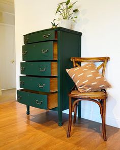 a wooden chair sitting next to a tall green cabinet with drawers on it's sides