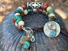 "This Third Eye bracelet is rich in symbolism. It features a Sterling button with a 3rd eye and Turquoise teardrop that doubles as the button closure.  In this two strander, I used Natural Turquoise wheels,  Fossil Coral and beautiful faceted Carnelian beads. One strand showcases a Indian Dzi bead bringing protection and positive energy to the wearer.  A Sterling \"Om\" and a \"Hamsa\" charm dangle from the link bringing their own positive vibe together. Loop the dark brown leather through the button to close.   When you purchase, please note your wrist size.  I will adjust to assure a perfect fit!" Bohemian Gemstone Bracelets For Meditation, Bohemian Style Gemstone Bracelets For Meditation, Symbolic Beaded Bracelets With Natural Stones For Meditation, Artisan Handmade Bracelets For Meditation, Spiritual Gemstone Beads Bracelets For Festivals, Symbolic Natural Stone Beaded Bracelets With Round Beads, Symbolic Beaded Bracelets With Natural Round Beads, Symbolic Beaded Bracelets With Natural Stones, Symbolic Natural Stone Beaded Bracelets