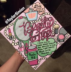 a hand holding up a pink graduation cap with the words beauty shop written on it