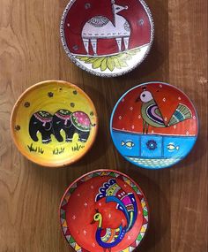 three colorful bowls sitting on top of a wooden table with animals painted on the lids