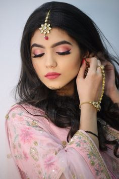 a woman with long black hair wearing a pink sari and gold jewelry on her head